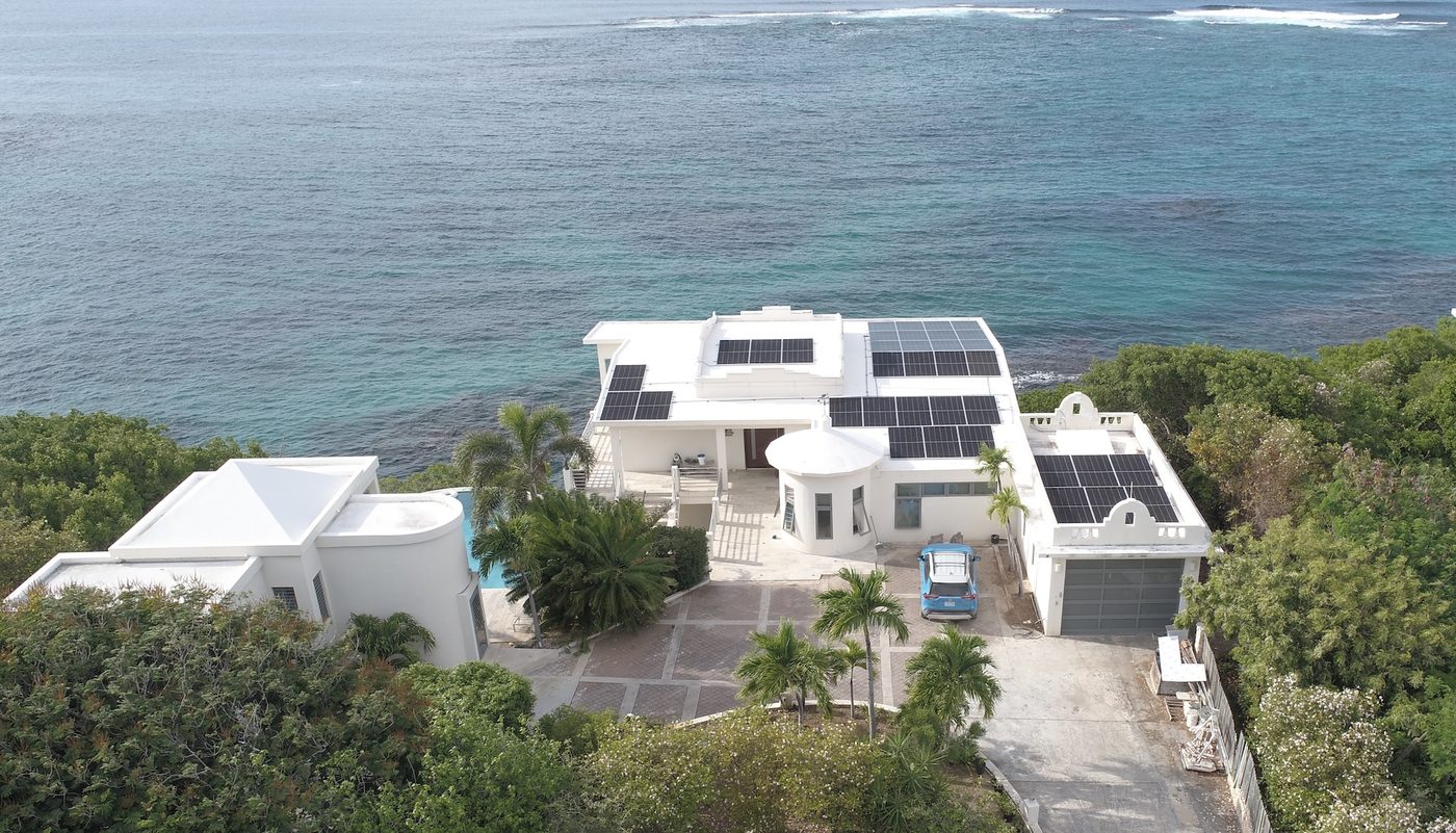 Aerial view of Caribbean villa with full solar panel coverage beside the ocean
