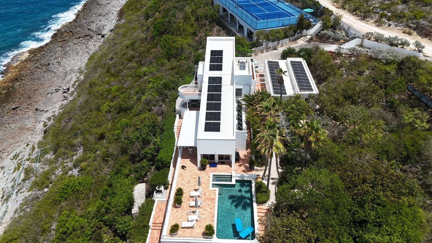 Aerial view of cliff-top villa with solar panels and pool
